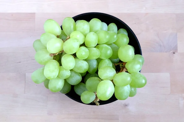 Bagas de uva verde madura em preto tigela redonda vista superior — Fotografia de Stock