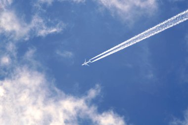 Passenger jet flying in blue sky with clouds leaving white trail clipart