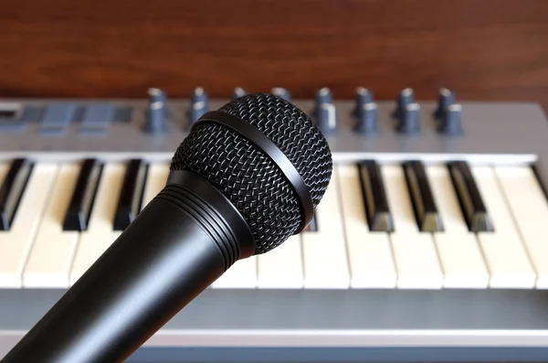 Black vocal microphone closeup against electronic synthesizer keyboard — Stock Photo, Image