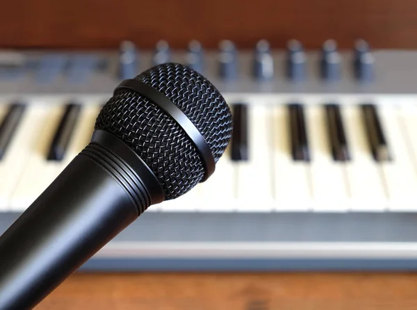 Black vocal microphone closeup against electronic synthesizer keyboard — Stock Photo, Image