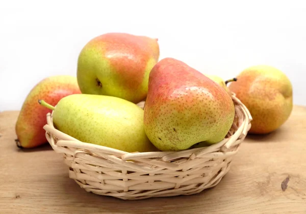 Red and yellow pears lays in wicker basket on brown wooden table front view closeup — Stock Photo, Image