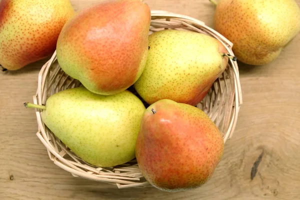 Rode en gele peren legt in rieten mand op bruin houten tafel bovenaanzicht closeup — Stockfoto