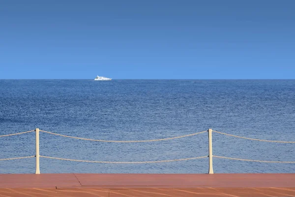 White boat float far on the sea horizon view from the wooden pier in cloudless day — Stock Photo, Image