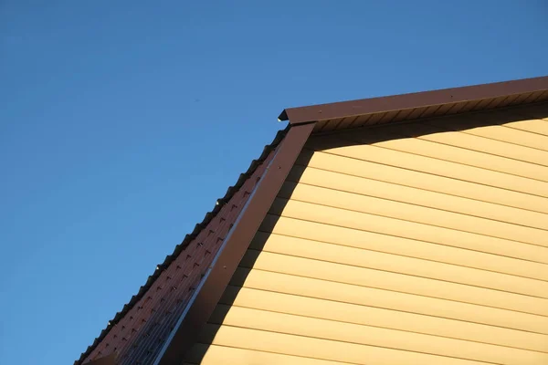 Součástí venkovský dům zdi pokryté žlutým vlečky a hnědá kovová střecha čelní pohled — Stock fotografie