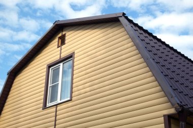 Sarı siding ve kahverengi metal çatı önden görünüm ile kaplı ülke ev duvar parçası