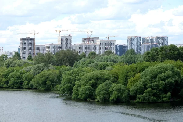 Construcción de un nuevo edificio en un nuevo distrito tras otro río sobre el cielo con nubes blancas en el día de verano — Foto de Stock