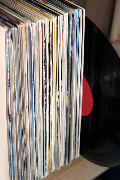 Stack of many vinyl records in old color covers on wooden shelf side view