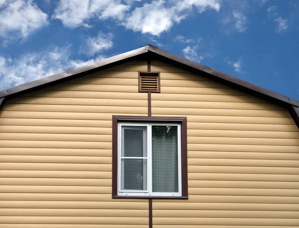 Part of rural house wall covered with yellow siding and brown metal roof front view — Stock Photo, Image