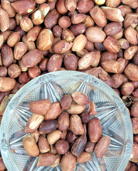 Gebratene Erdnüsse in kleiner Glasschüssel und viele geröstete Erdnussfrüchte als Hintergrundansicht — Stockfoto