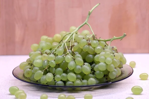 Trossen van rijpe groene druif in transparante plaat op keuken tabel vooraanzicht closeup — Stockfoto