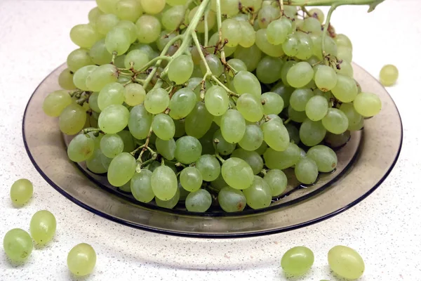 Des grappes de raisin vert mûr dans une assiette transparente sur la table de cuisine gros plan — Photo