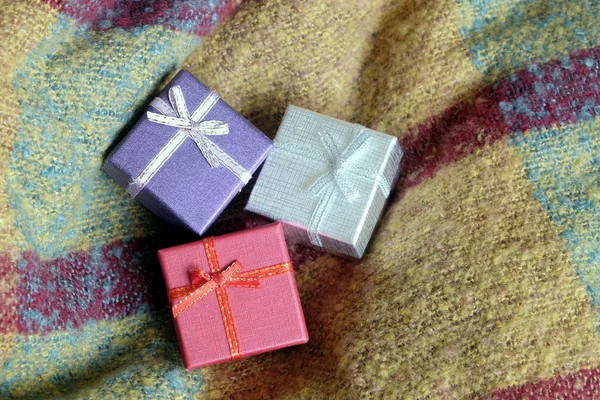 Tres regalos navideños en pequeñas cajas de colores, cubiertas con cinta, sobre un fondo de tela de lana —  Fotos de Stock