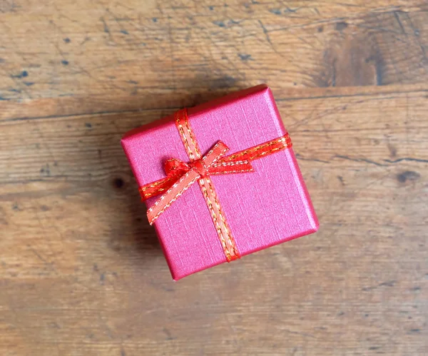 Pequeño regalo de vacaciones en caja de color rojo cuadrado, cubierto con cinta con lazo en vista superior de fondo de madera — Foto de Stock