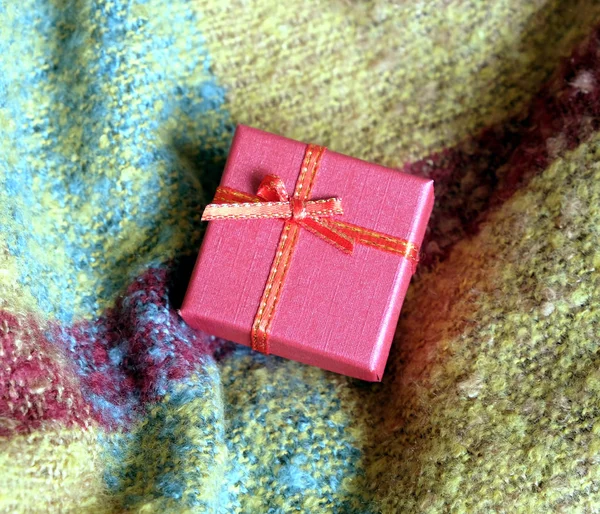 Bodegón con regalo navideño en una pequeña caja de color rojo, cubierta con cinta con lazo, sobre un fondo de tela de lana —  Fotos de Stock