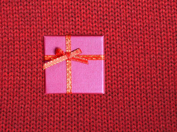 De gift van de vakantie van Kerstmis in kleine kleurvak bedekt met lint met strik tegen rode achtergrond van wollen gebreide stof bovenaanzicht — Stockfoto