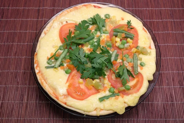 Аппетитная пицца с помидорами, кукурузой и зеленым горошком на круглой тарелке на коричневом соломенном коврике — стоковое фото