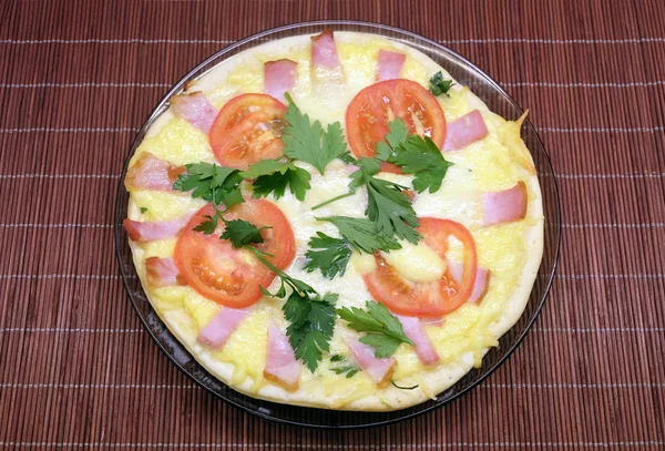 Аппетитная пицца с помидорами, кукурузой и зеленым горошком и беконом на круглой тарелке на коричневой соломенной циновке — стоковое фото