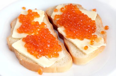 Tereyağı ve beyaz ekmek üzerinde kırmızı havyar ile iki sandviç yatıyor yuvarlak tabakta beyaz arka plan üzerinde üstten görünüm izole