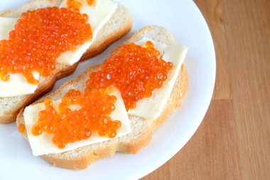 Kırmızı somon havyar üzerinde beyaz ekmek ve tereyağı ile iki sandviç yatıyor ahşap arka plan üstten görünüm üzerinde beyaz yuvarlak plaka üzerinde