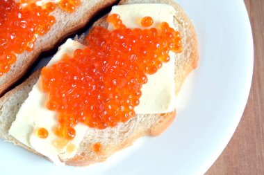 Kırmızı somon havyar üzerinde beyaz ekmek ve tereyağı ile iki sandviç yatıyor ahşap arka plan üstten görünüm üzerinde beyaz yuvarlak plaka üzerinde