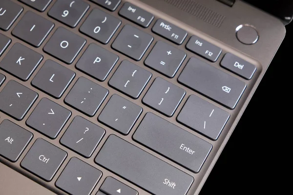 Part of opened laptop with keyboard, touchpad and empty mirror screen of black opened laptop isolated on black background top view closeup