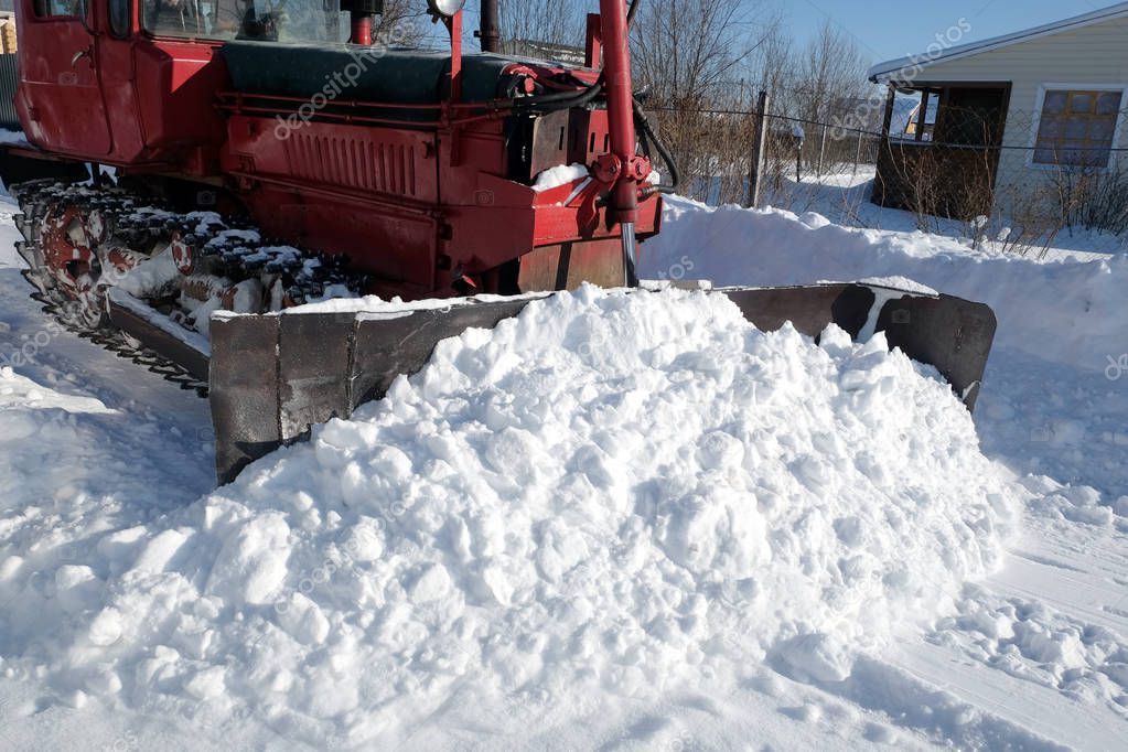 Diesel caterpillar tractor cleans the road from snow in a country village on a bright sunny day side view closeup