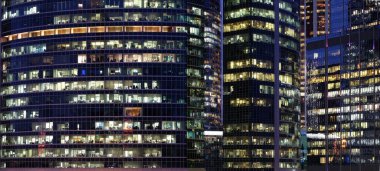 Şehir merkezinde panoramik pencereleri olan modern ofis binalarının cam duvarları gece panoramik çalışan insanlarla dolu.