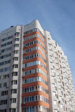 Çok katlı çok katlı bir apartman bloğunun ön cephesi. Mavi gökyüzü üzerinde birçok apartman dairesi var. Altında hafif bulutlar var.