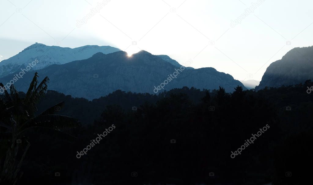 Sunset with last sun rays above high light blue mountain silhouettes in haze with stepped lighting