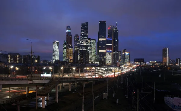 遠くに行く多くの鉄道線路のある街の風景 夕方には照明窓のあるモスクワ市の塔のある陸橋や高層ビルの車 — ストック写真