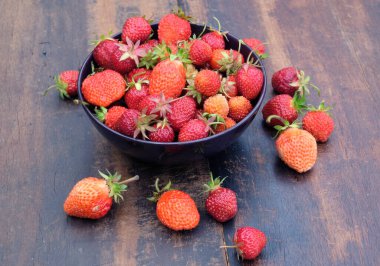 Eski ahşap masa yüzeyinde toplanmış taze, iştah açıcı çileklerle dolu bir hayat. Arka plan manzarası yakın.