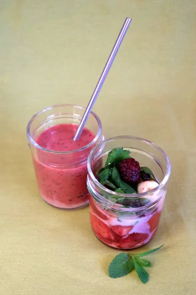 Non-alcohol fruit smoothie cocktails with strawberry and blackberry in yogurt with mint leaves in the transparent wine glasses on green background front view close up