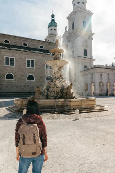 Viaggiatore ragazza con uno zaino vicino alla fontana e alla cattedrale — Foto Stock