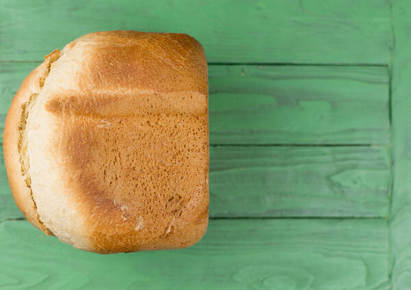 A loaf of homemade white bread on a green wooden background.