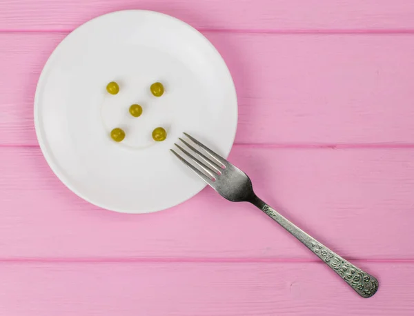 Il concetto di fame, bulimia. Pochi piselli su un piatto bianco e una forchetta . — Foto Stock