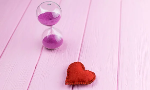 Outgoing love in time. Hourglass and heart on a pink background.