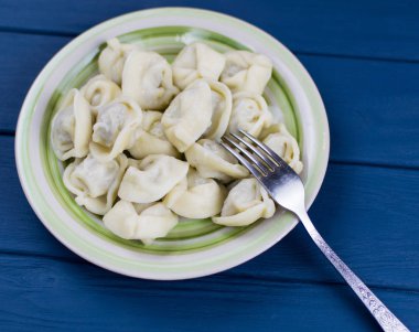 Üzerinde koyu mavi ahşap renkli bir tabağa haşlanmış mantı.