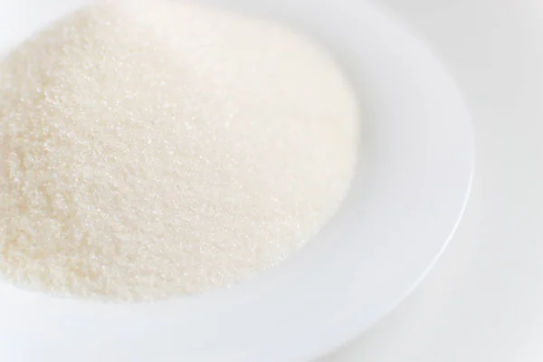 Azúcar en un plato blanco sobre un fondo blanco . — Foto de Stock