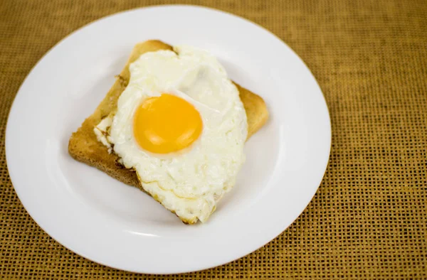 Toast avec oeuf frit sur une assiette blanche sur un fond brun . — Photo