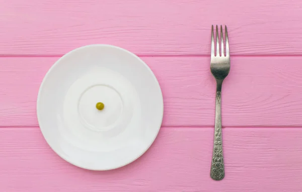 Il concetto di fame, bulimia. Pisello su un piatto bianco e una forchetta . — Foto Stock