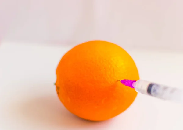 Het concept van niet-natuurlijke producten, GGO. Spuit en sinaasappel op een witte achtergrond. — Stockfoto