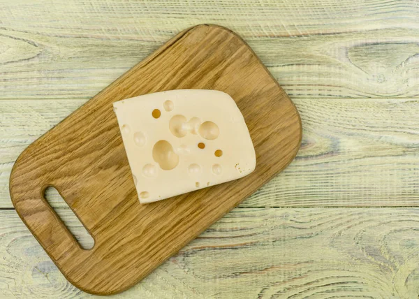 A piece of cheese with large holes on a wooden cutting board. — Stock Photo, Image