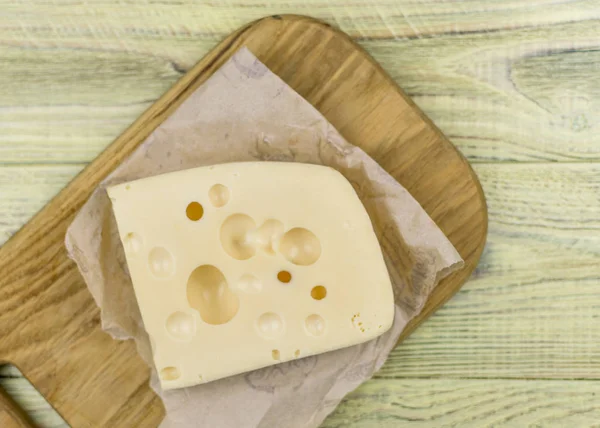 Bir parça peynir bir ahşap kesme tahtası üzerinde büyük delikli. — Stok fotoğraf