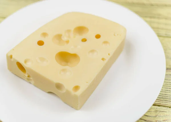 Un trozo de queso con agujeros en un plato blanco . — Foto de Stock