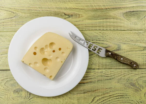 Bir parça peynir delikleri ve beyaz bir plaka üzerinde kesim için bir bıçak ile. — Stok fotoğraf