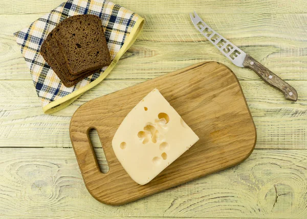 Bir dilim peynir kesme tahtası ve bir ahşap yüzey yanındaki siyah ekmek üzerinde. — Stok fotoğraf