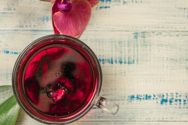 Ahşap zemin üzerinde cam bir fincanda kırmızı orkideli meyve çayı..