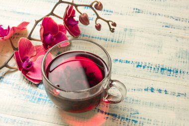 Ahşap zemin üzerinde cam bir fincanda kırmızı orkideli meyve çayı..