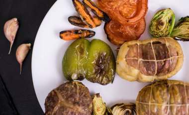 Beyaz tabakta ızgara sebzeli pirzola ve siyah bir arka plan..