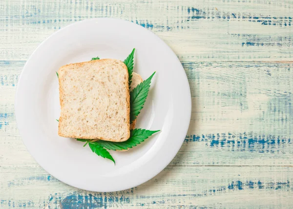Marijuana and food. A sandwich with marijuana leaves. The use of cannabis in the manufacture of food. The concept of increasing appetite after consuming marijuana. — Stock Photo, Image